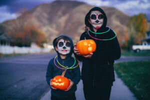 Two young children, a boy and a girl, are dressed as a calaveras skeletons for Halloween. They are ready to trick or treat for candy while holding illuminated Jack O' Lanterns in a local residential neighborhood. Image taken in Utah, USA.