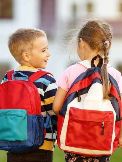 Two young students wearing colorful backpacks stand together outdoors.